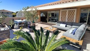 An outdoor patio area with a sofa, table, and chairs, surrounded by potted plants and a pergola.