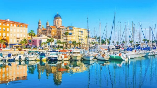 A marina with boats docked, a prominent building with a dome, and a clear blue sky.