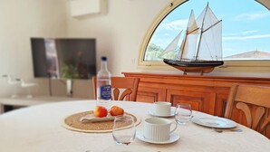 A dining table set with plates, cutlery, and glasses, a bottle of water, and a model ship on a window sill.