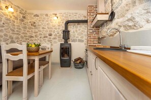 Une cuisine rustique avec un mur en pierre, un poêle à bois, une table en bois avec des chaises et un évier.