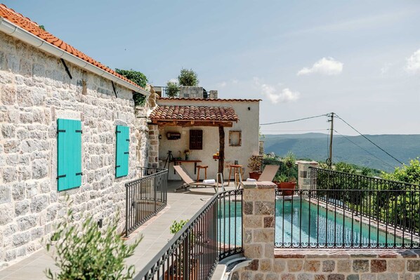 Un bâtiment en pierre avec un toit en tuiles, une piscine et une vue sur les montagnes.