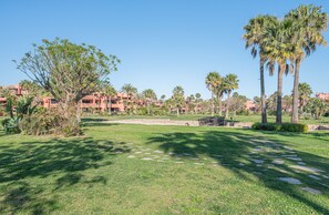 A well-maintained grassy area with palm trees and a stone pathway leading to a building complex. - BEAUTIFUL HOUSE 5 MINUTES WALKING FROM THE BEACH (ESTEPONA)