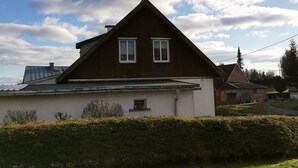 Una casa con techo inclinado, dos ventanas y una pequeña construcción adosada.