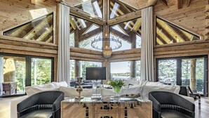 A spacious living area with a large wooden ceiling, a central glass table, and black leather chairs. - 7 bed 6 bath cottage on Lake Muskoka (Gravenhurst)