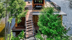 A wooden cabin with a deck and a small balcony, surrounded by trees and water. - 7 bed 6 bath cottage on Lake Muskoka (Gravenhurst)