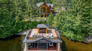 A wooden cabin with a dock, surrounded by dense forest and a body of water. - 7 bed 6 bath cottage on Lake Muskoka (Gravenhurst)