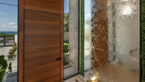 A modern interior with a wooden door, a glass wall reflecting the sky, and a bench. - Luxurious 5 BR Ocean Front Home. Epic Views! (Isla Mujeres)