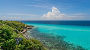 A coastal landscape with clear turquoise waters, rocky terrain, and lush greenery. - Luxurious 5 BR Ocean Front Home. Epic Views! (Isla Mujeres)
