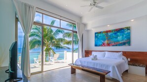 A hotel room with a large window, a bed, a bench, and a painting on the wall. - Luxurious 5 BR Ocean Front Home. Epic Views! (Isla Mujeres)