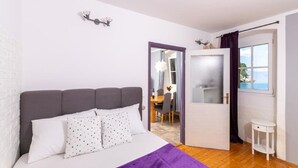 Una camera da letto con un letto, una coperta viola, un cuscino bianco e un piccolo comodino bianco.