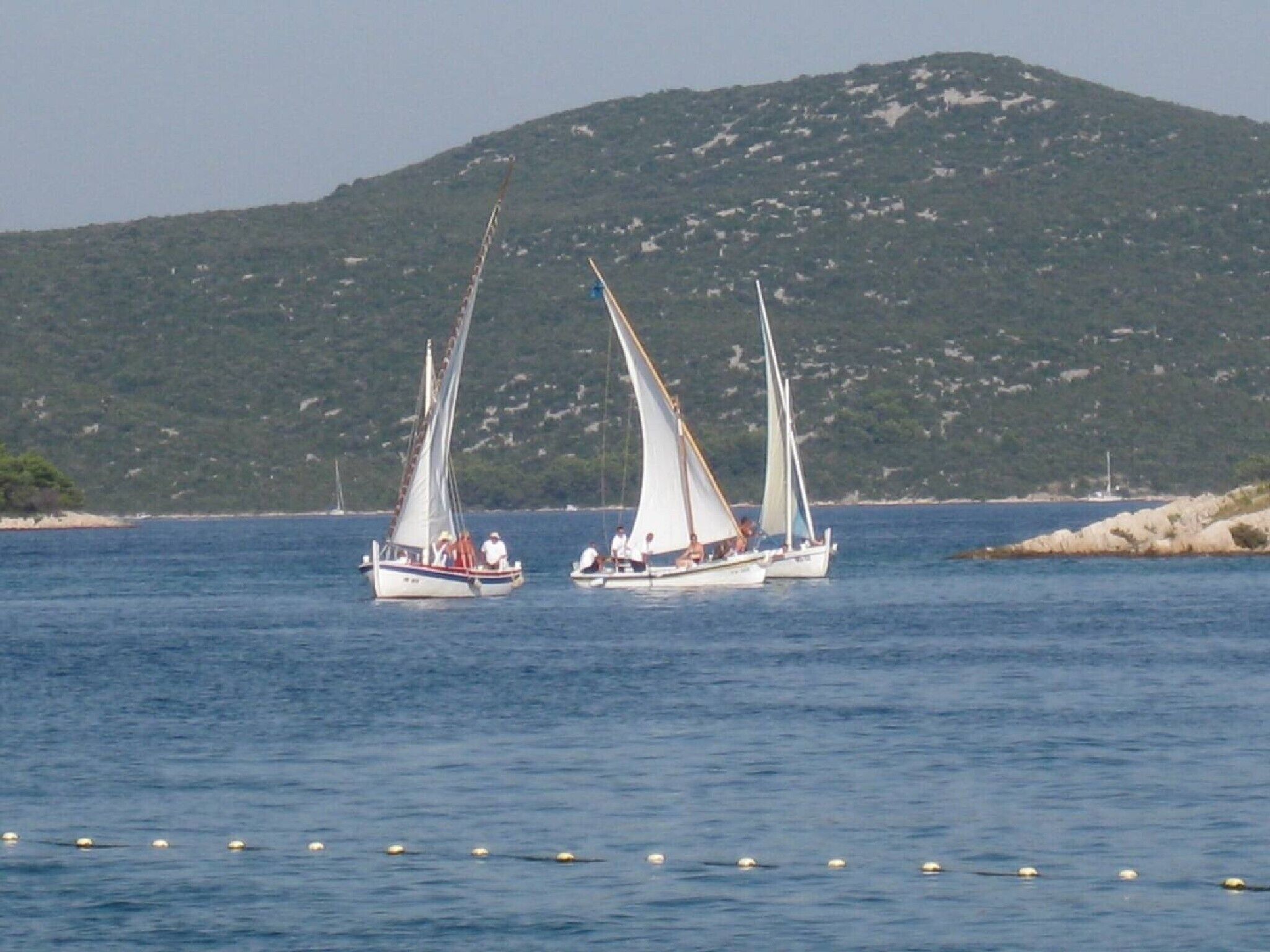 Three sailboats on calm waters with a mountainous backdrop.