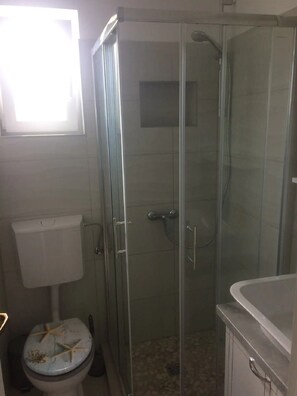 Ett badrum med en dusch som är avskärmad med glasväggar, en toalett och ett handfat.