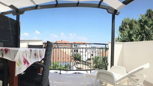 A covered outdoor area with a table and chairs, a view of buildings and trees, and a railing. - Apartments Paula - One Bedroom Apartment with Terrace 2 (Jezera)