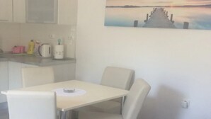 Una habitación moderna con una cama, una mesa de comedor con sillas, una zona de cocina y un cuadro de un atardecer sobre el agua.