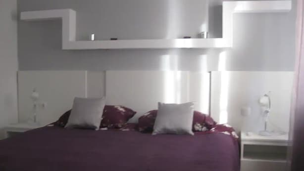 Un dormitorio con cama, dos mesitas de noche y una pared blanca con estantes empotrados.