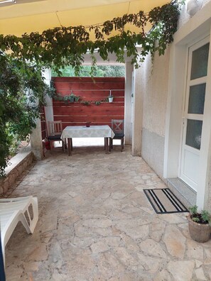 A stone-floored patio with a table and chairs, surrounded by potted plants and a wooden fence.
