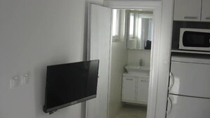 Cocina compacta con armarios blancos, un microondas y un televisor de pantalla plana montado en la pared.