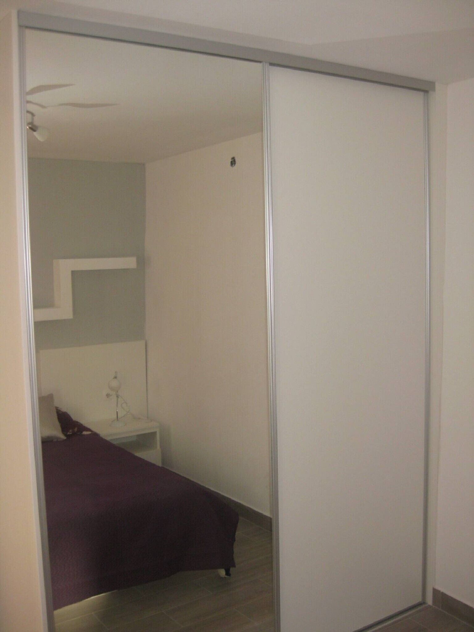 A bedroom with a bed, a bedside table, and a mirror.