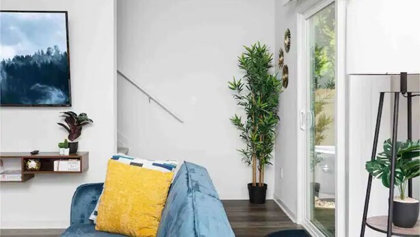 Un salon moderne avec un canapé bleu, un coussin jaune, une plante en pot et un tableau accroché au mur.