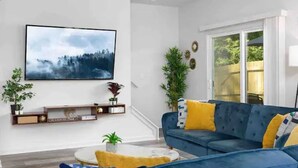 Un salon avec un canapé bleu, une table basse et un téléviseur fixé au mur.