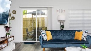 Un salon avec un canapé bleu foncé, des coussins jaunes, une lampe blanche et un téléviseur fixé au mur.