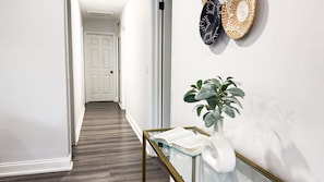 A hallway with a white door at the end, a plant on a glass table, and two woven baskets on the wall.