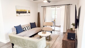 Een moderne woonkamer met een bank, fauteuil, salontafel en een flatscreen televisie aan de muur.
