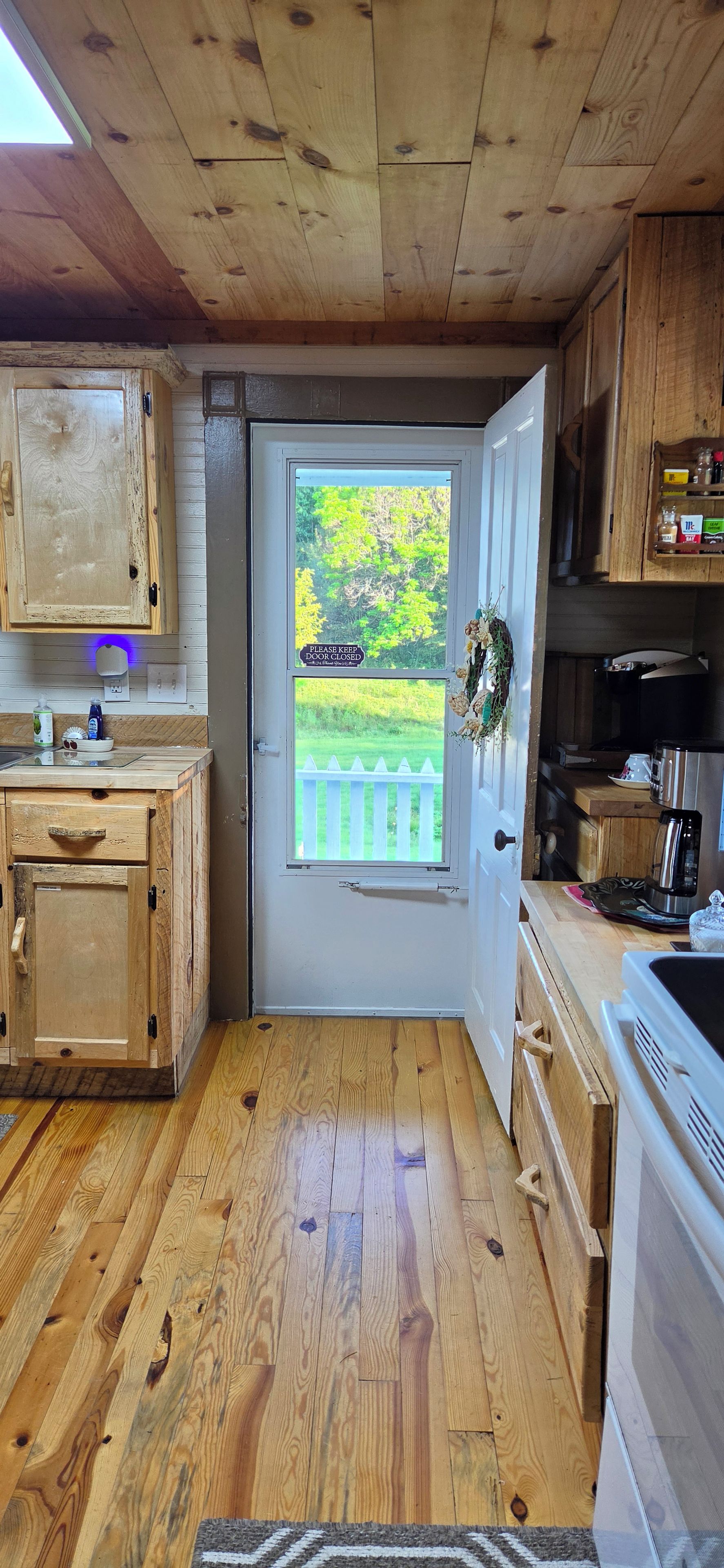 Un intérieur en bois avec une porte donnant sur une vue d’une clôture blanche et d’une végétation luxuriante.