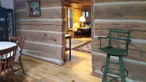 Ein Holzblockhaus-Interieur mit Esstisch, Stühlen, einer Lampe und einem Bild an der Wand.