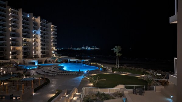 A nighttime view of a hotel with a swimming pool, outdoor seating, and a view of the city skyline.