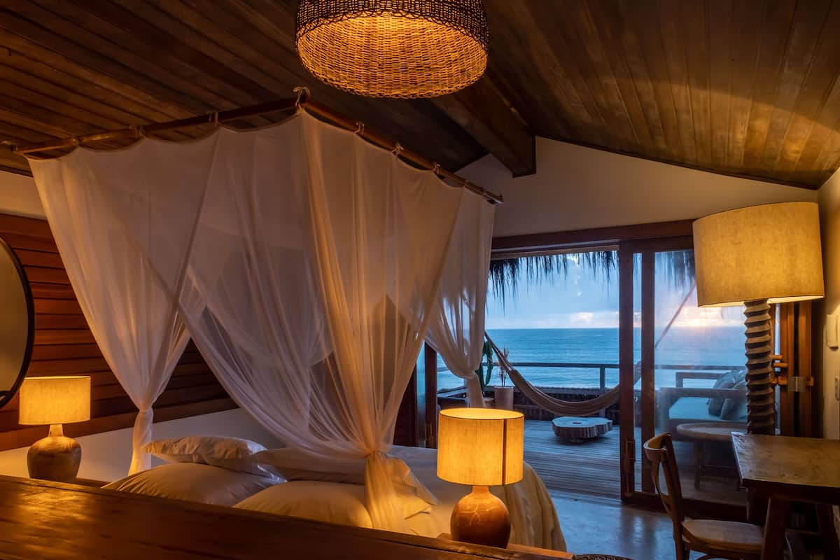 Een slaapkamer met een hemelbed, een houten plafond en uitzicht op de oceaan.