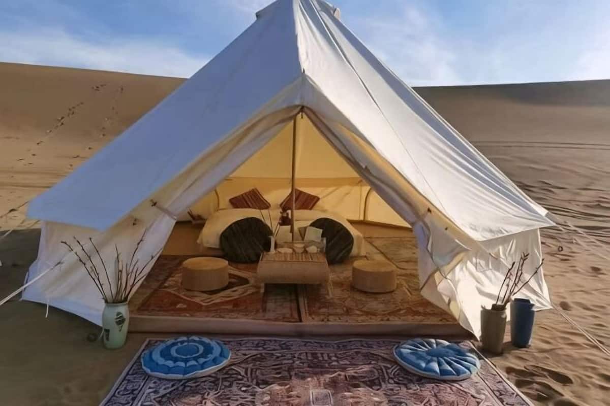 A tent with a bed, pillows, and a rug in a desert setting.