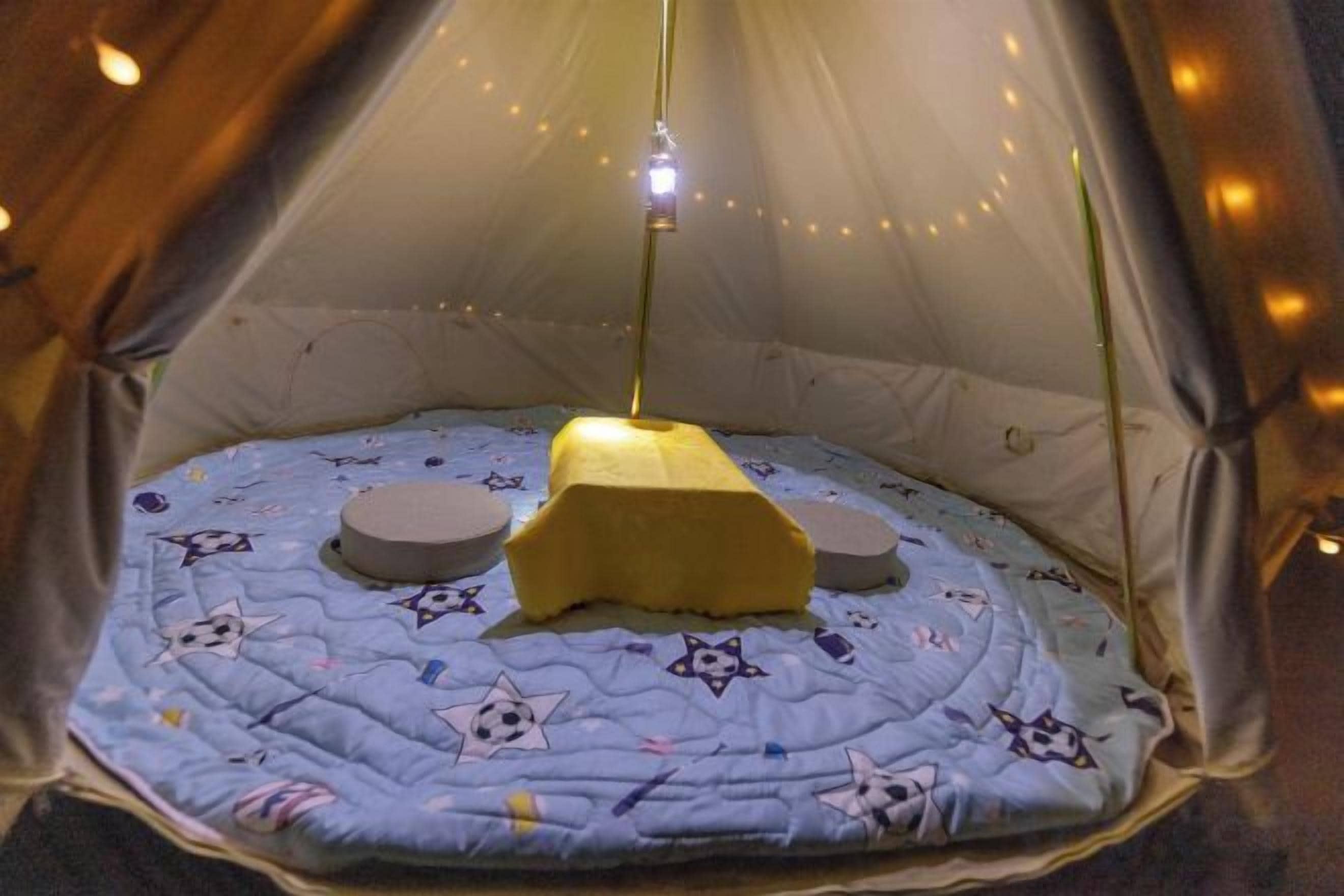 A tent with a bed, a hanging light, and a string of lights.