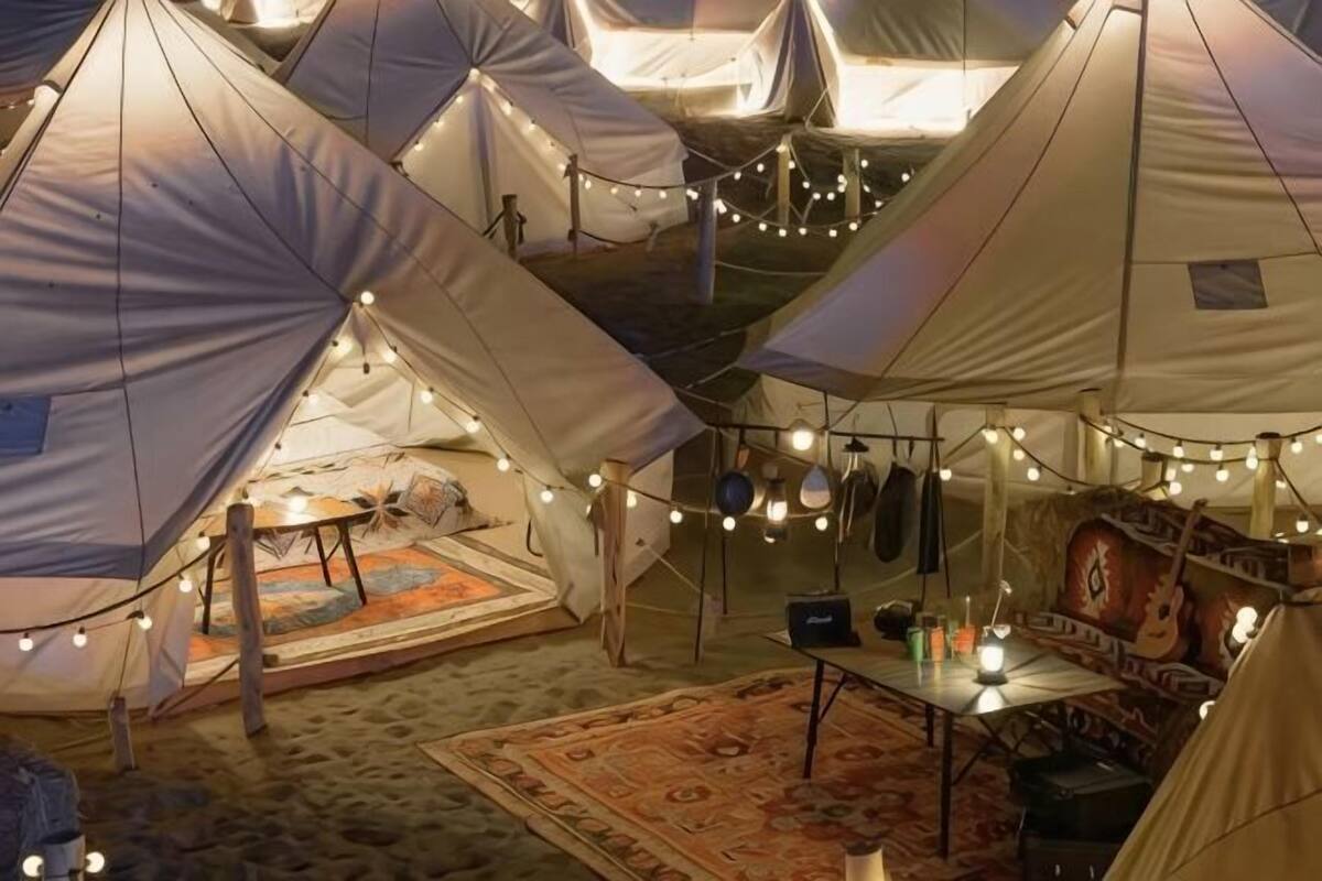 Multiple tents with string lights, a carpet, and a table with a guitar.