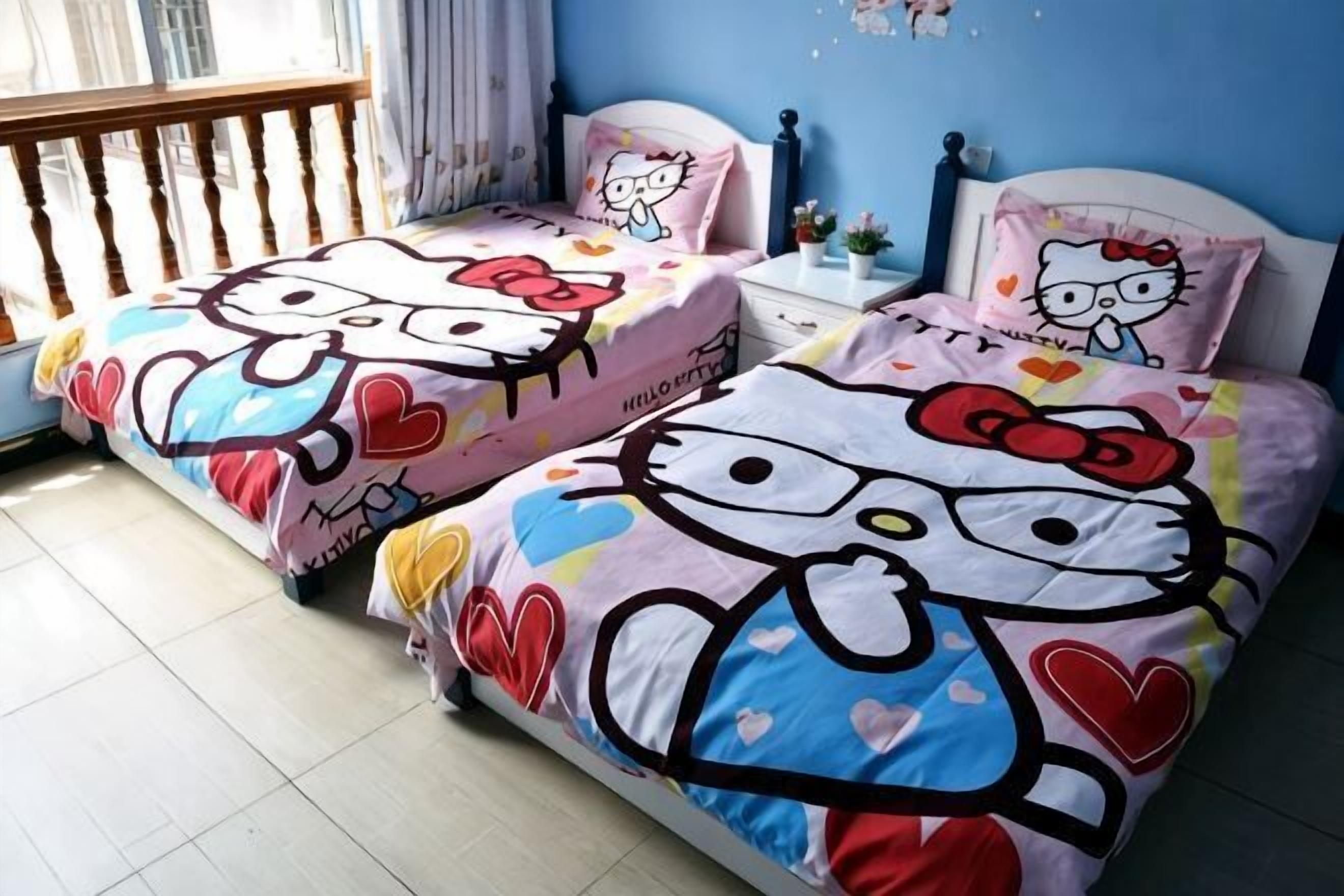 A room with two beds featuring Hello Kitty designs, a window with curtains, and a blue wall.