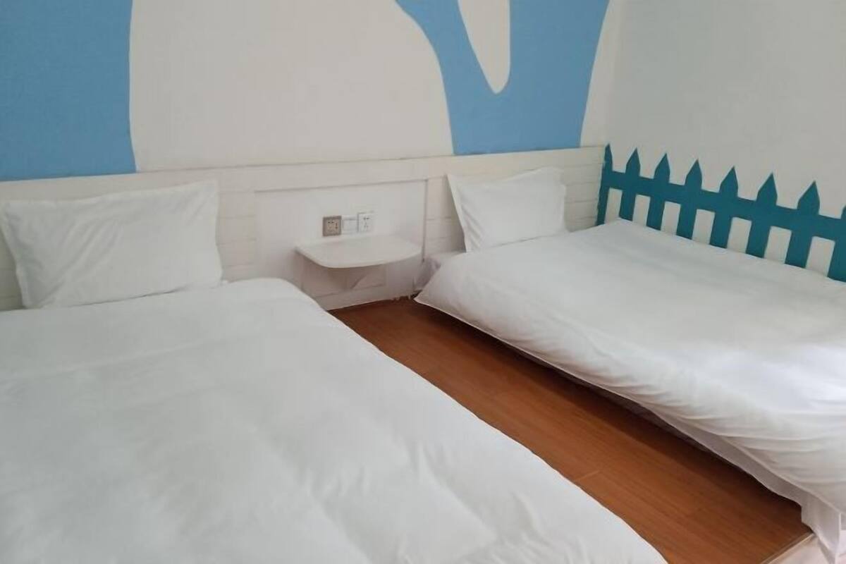 A hotel room with two single beds, a small bedside table, and a wall with a blue and white abstract design.