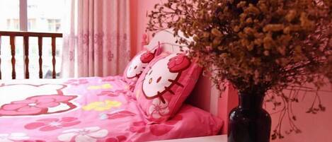 A bedroom with a pink floral bedspread, Hello Kitty pillows, and a vase with dried flowers.