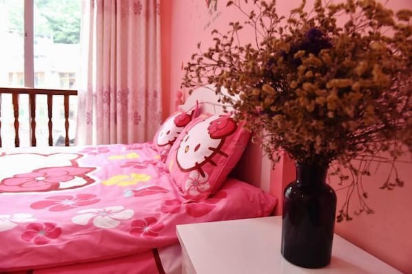 A bedroom with a pink floral bedspread, Hello Kitty pillows, and a vase with dried flowers.