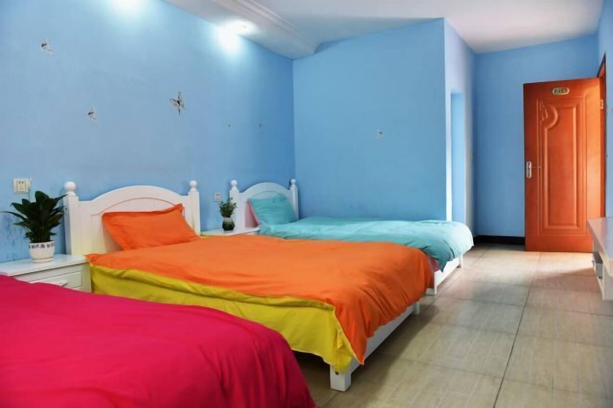 A room with two beds, a wooden door, and a small plant on the nightstand.