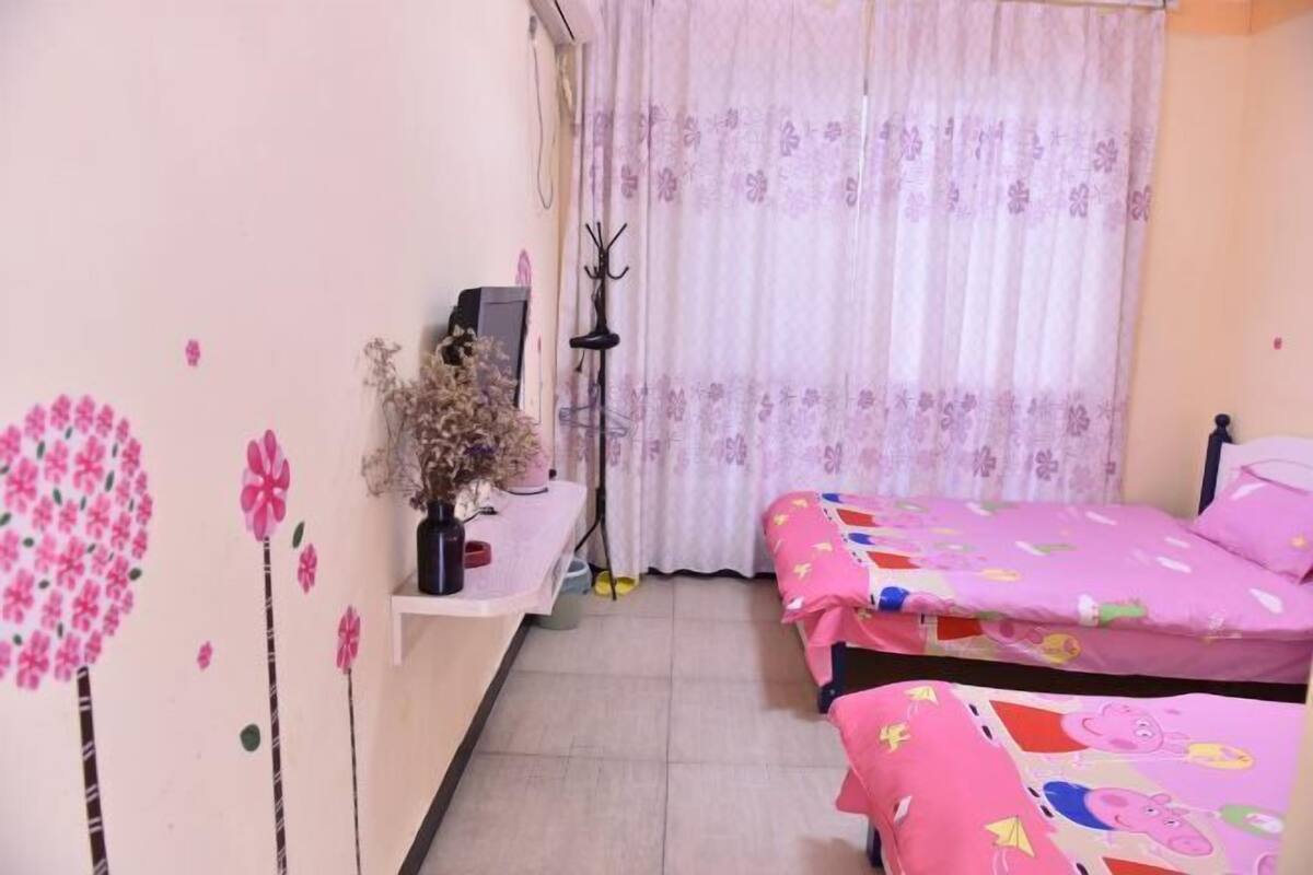A bedroom with two beds, a desk, a chair, a window with curtains, and a wall with a floral design.