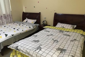 Two single beds with wooden headboards, a nightstand with a kettle, and a wall with small decorative items.
