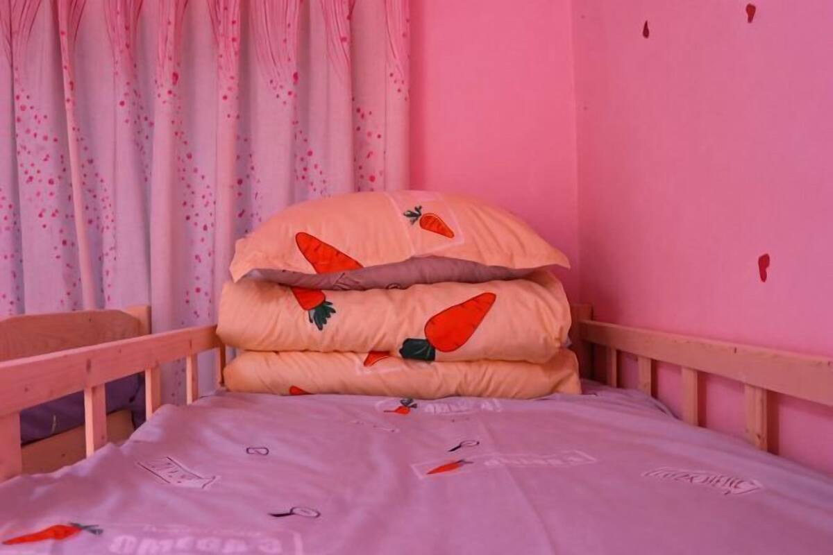 A pink room with a bed, a wooden headboard, and a window with curtains.