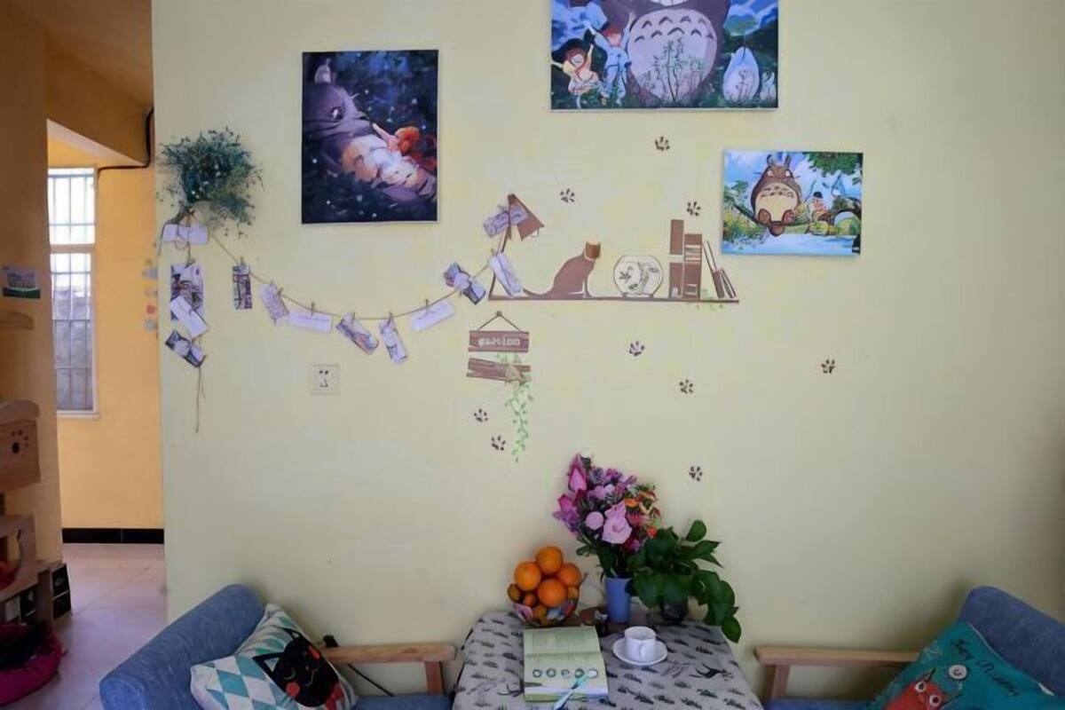 A room with a sofa, a small table with a vase of flowers, and wall decorations including framed pictures and a string of cards.