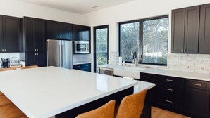 A modern kitchen with dark cabinets, a large island, and a view through the window. - Calistoga Vineyard House (Calistoga)