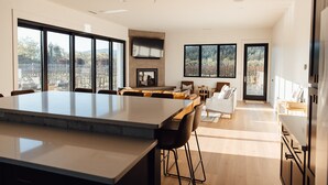 A modern kitchen with a large island, dining area with chairs, and a view of a vineyard through large windows. - Calistoga Vineyard House (Calistoga)