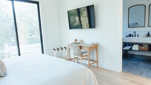 A bedroom with a large bed, a desk with a chair, a TV mounted on the wall, and a bathroom with a sink and mirror. - Calistoga Vineyard House (Calistoga)