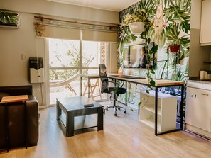 A modern kitchen with a large window, a dining area with a black table and chairs, and a living area with a sofa and a hammock. - Bright Studio with balcony, hammock and big desk (Paraná)