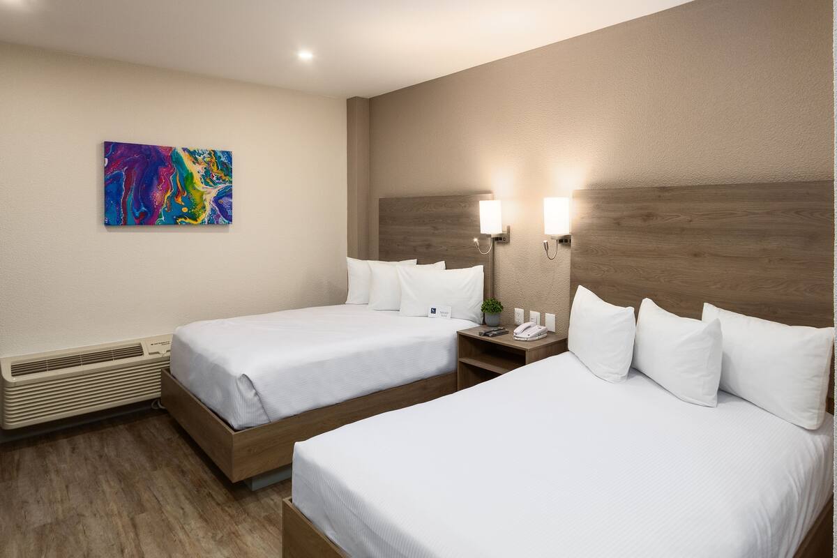 A hotel room with two beds, a heater, a nightstand with a lamp, and a colorful abstract painting on the wall.