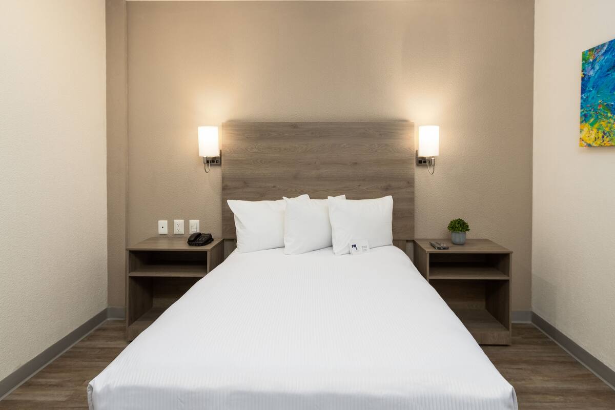 A hotel room with a large bed, two bedside tables, a wooden headboard, and two wall-mounted lights.