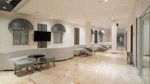 Un hall d’hôtel moderne avec un sol en marbre, des canapés blancs et des tables rondes.